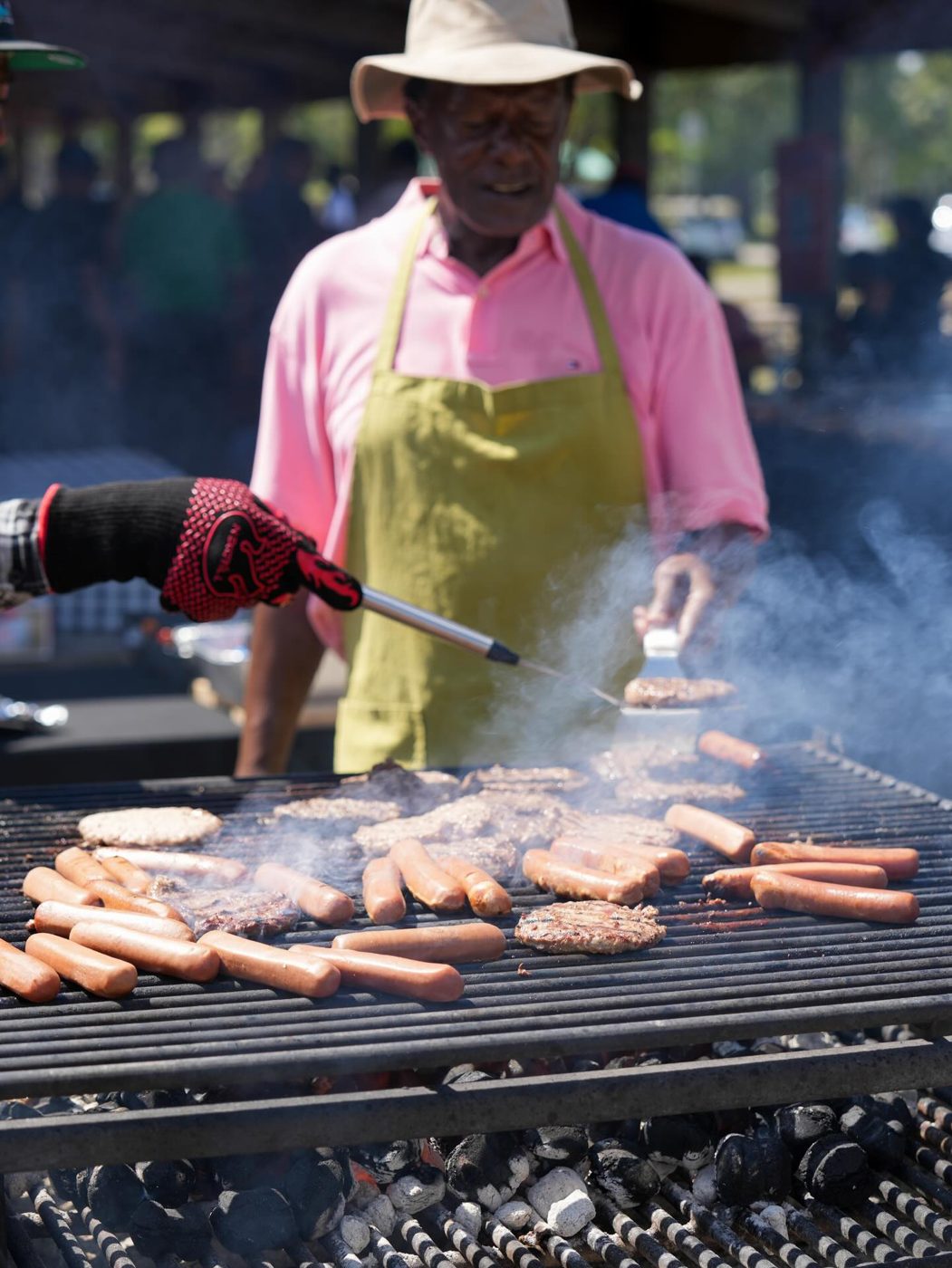 A volunteer cooking burgers and hot dogs on a grill