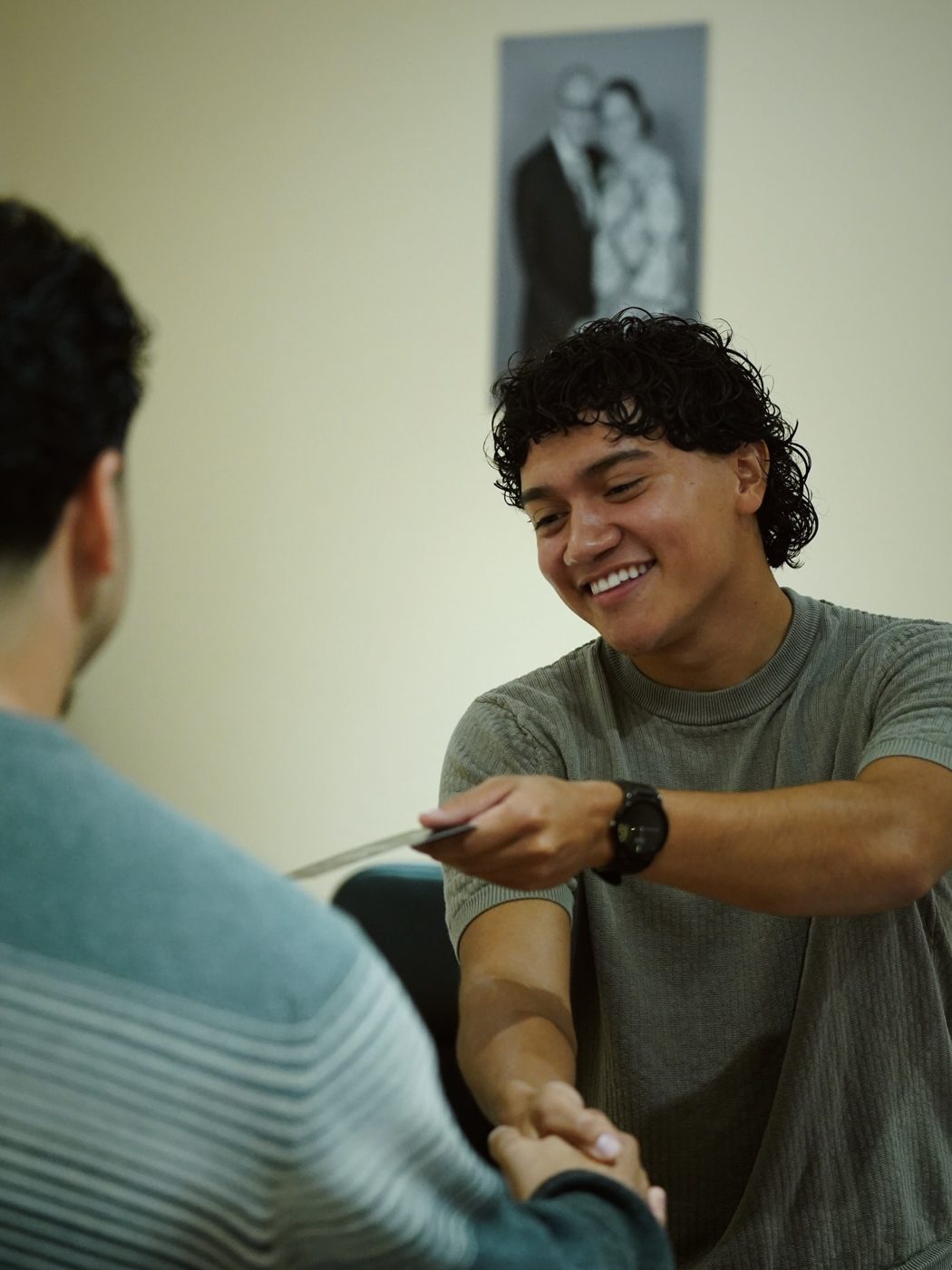 A smiling young man shaking hands and handing a card to a guest inside the church