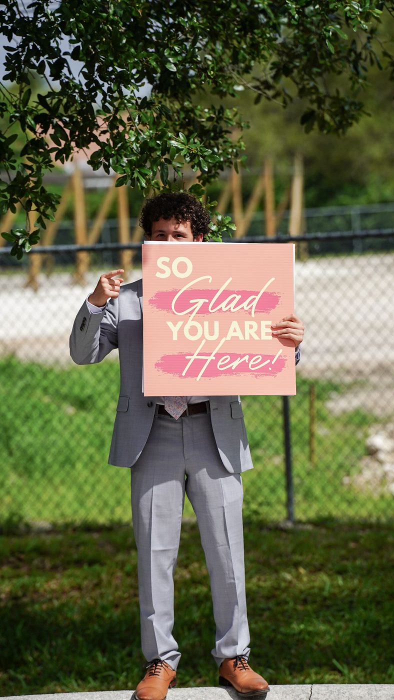 A greeter holding a sign that reads So Glad You Are Here