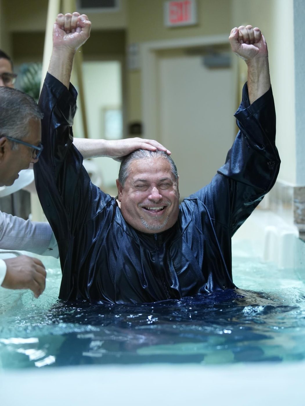 A man celebrating with both arms raised in the baptism tank